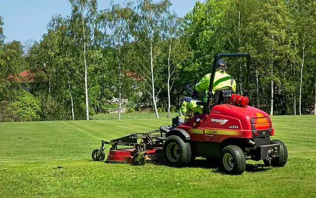Red commercial riding mower cutting a wide grass field