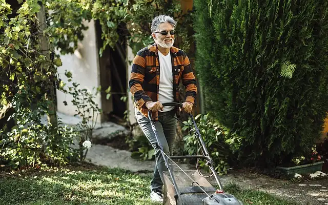Man pushing a gas lawn mower across a backyard