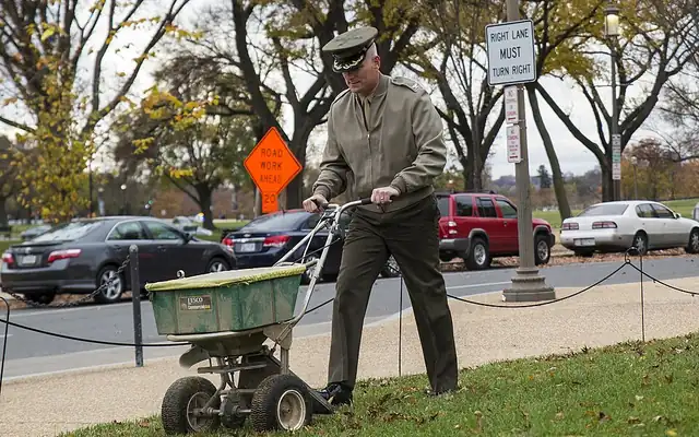 Man spreading grass seed on a lawn with a push spreader