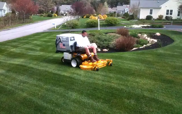 Lawn care worker on a zero-turn mower in a front yard