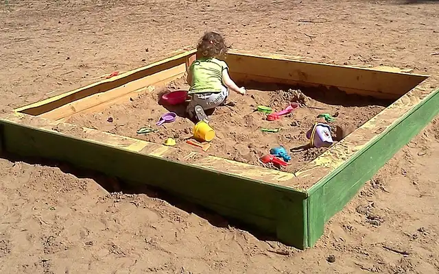 Child playing in a wooden backyard sandbox